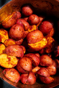 raw potatoes tossed with spices and olive oil in a mixing bowl