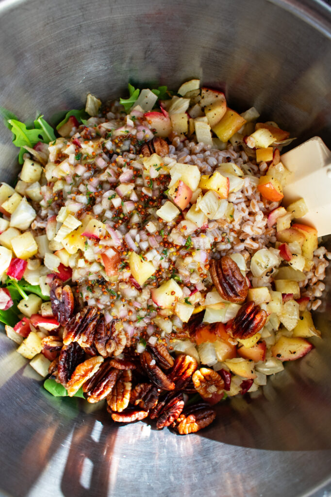 salad ingredients in a mixing bowl - arugula, roasted apples, roasted fennel, toasted pecans, and maple mustard vinaigrette