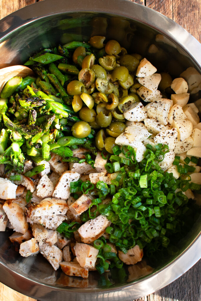 grilled chicken, grilled asparagus, castelvetrano olives, fresh mozzarella, and green onions in a mixing bowl