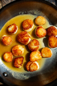seared scallops in a skillet with lemon butter sauce