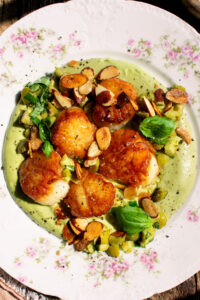 a plate of seared scallops over whipped cauliflower with olives and toasted almonds