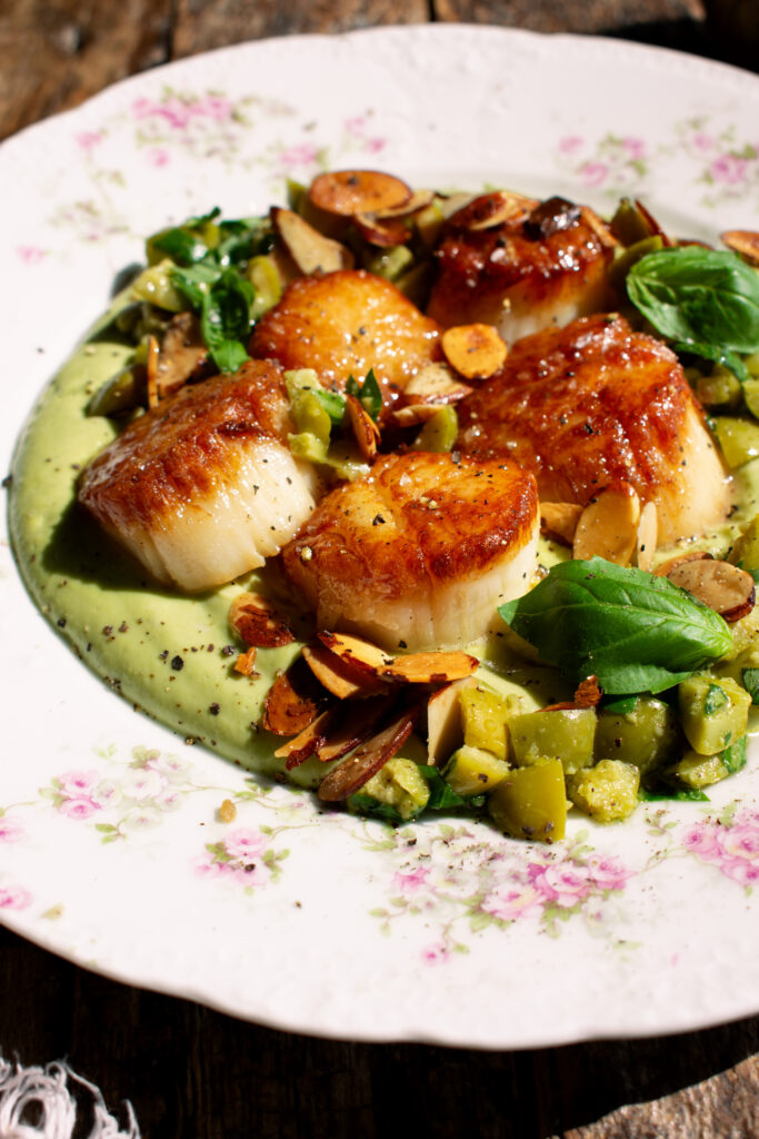 a plate of seared scallops over whipped cauliflower with olives and toasted almonds