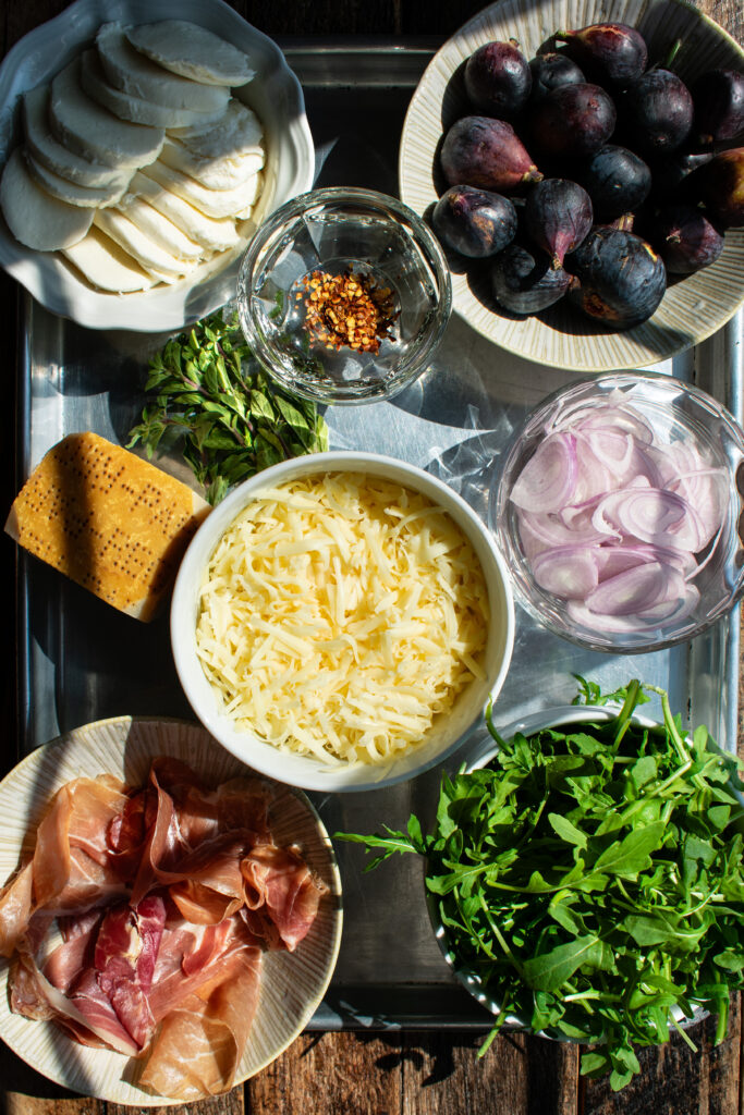 pizza ingredients: figs, shallots, arugula, mozzarella, fontina, prosciutto, parmesan, oregano, and red pepper flakes