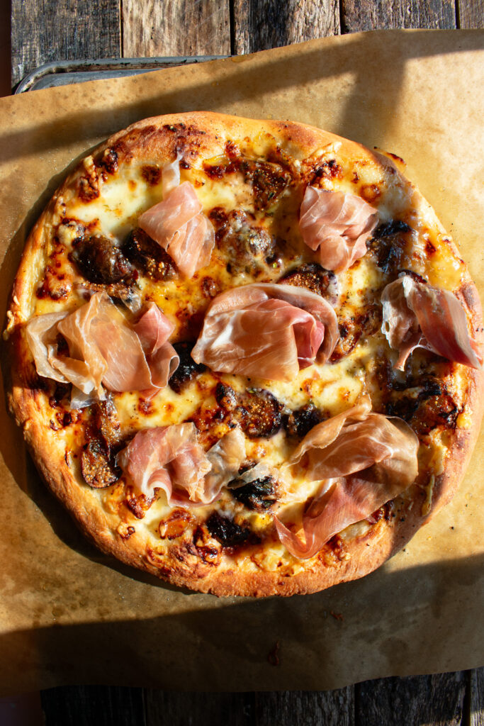 pizza out of the oven topped with figs, melted cheese, and prosciutto