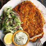 plate of sliced walnut crusted chicken, fennel slaw, herb mayo, and a lemon half