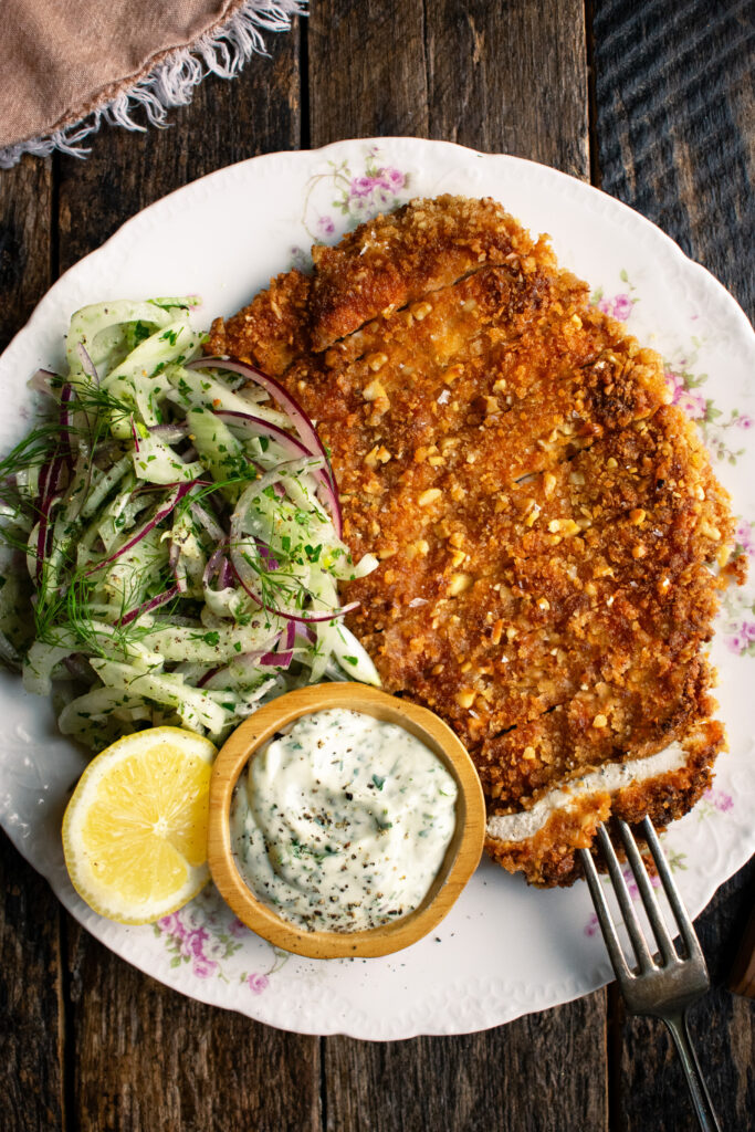 plate of sliced walnut crusted chicken, fennel slaw, herb mayo, and a lemon half