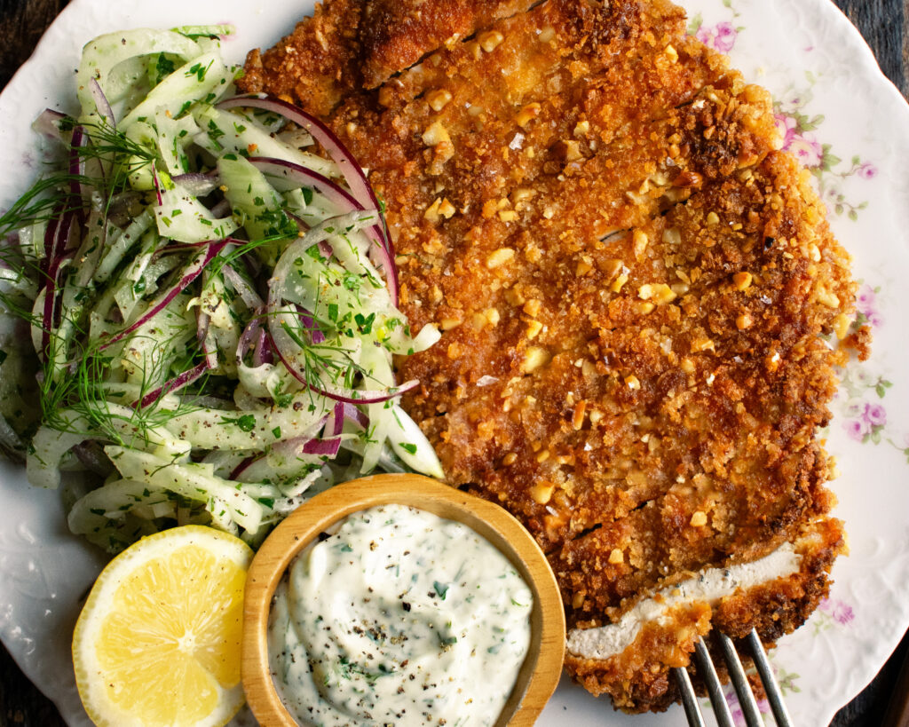 plate of sliced walnut crusted chicken, fennel slaw, herb mayo, and a lemon half